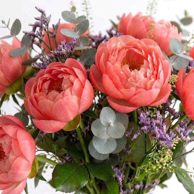 Hand-tied coral peony and limonium bouquet in a vase.