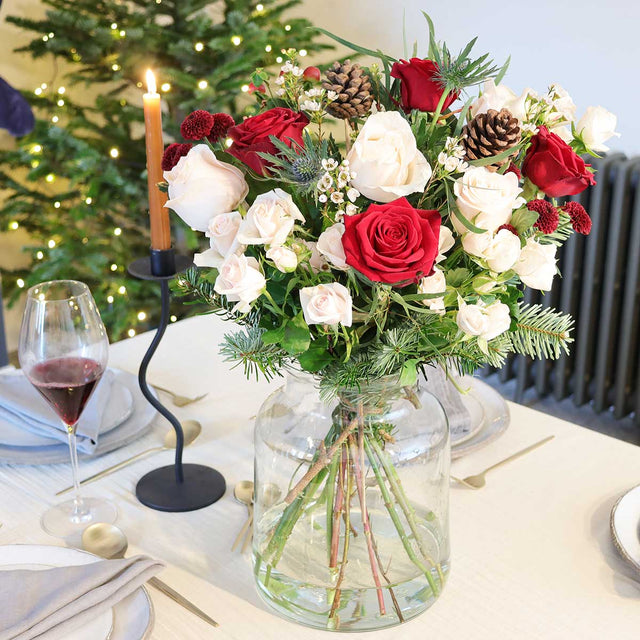 The Noel hand-tied Christmas bouquet in a vase set on a table.